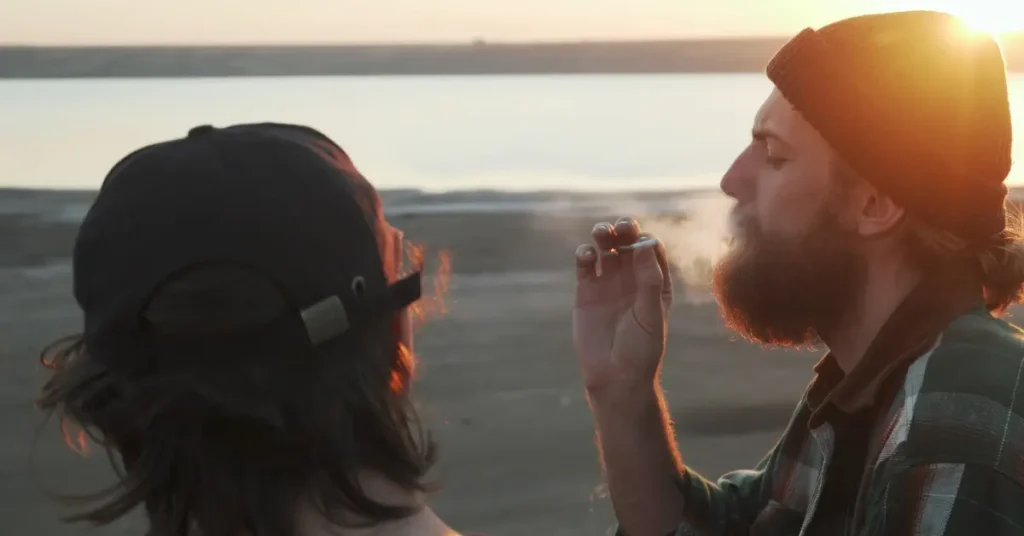 two adult men smoking cannabis overlooking a lake