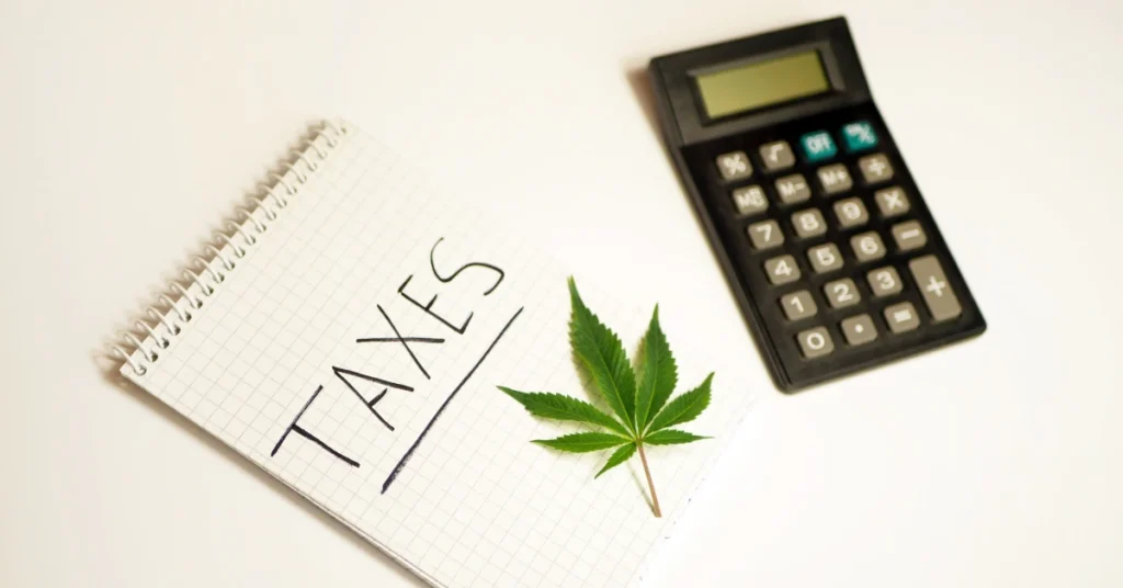 marijuana leaf on top of a notepad with the word taxes written next to a calculator.
