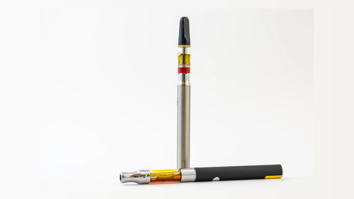 A cannabis vape cartridge resting beside a 510-thread battery with oil visible inside the cartridge.