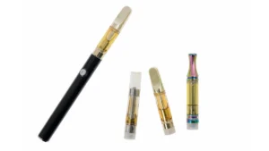 A cannabis vape cartridge with oil visible inside resting beside a vape battery on a plain surface.