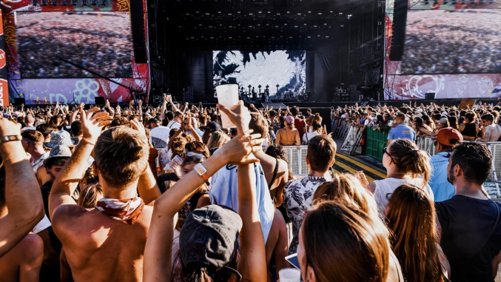 A summer music festival crowd at golden hour with hands raised toward the stage.