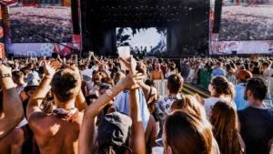 A summer music festival crowd at golden hour with hands raised toward the stage.