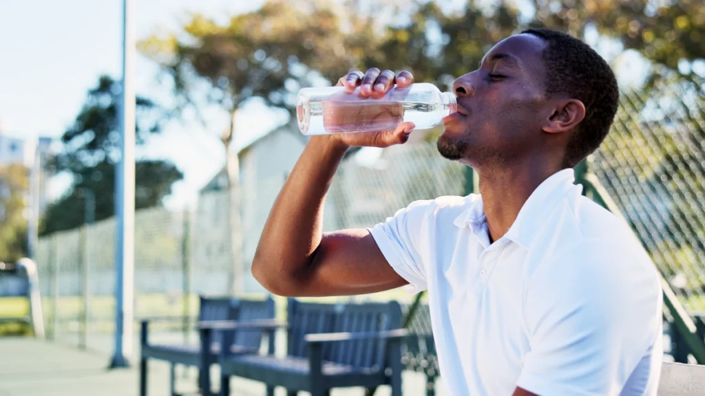 Person relaxing outdoors in summer heat drinking from a water bottle