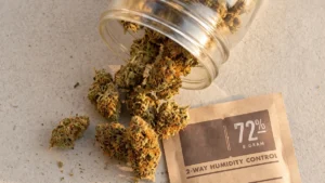 Dry cannabis flower beside an open glass storage jar and a two-way humidity pack